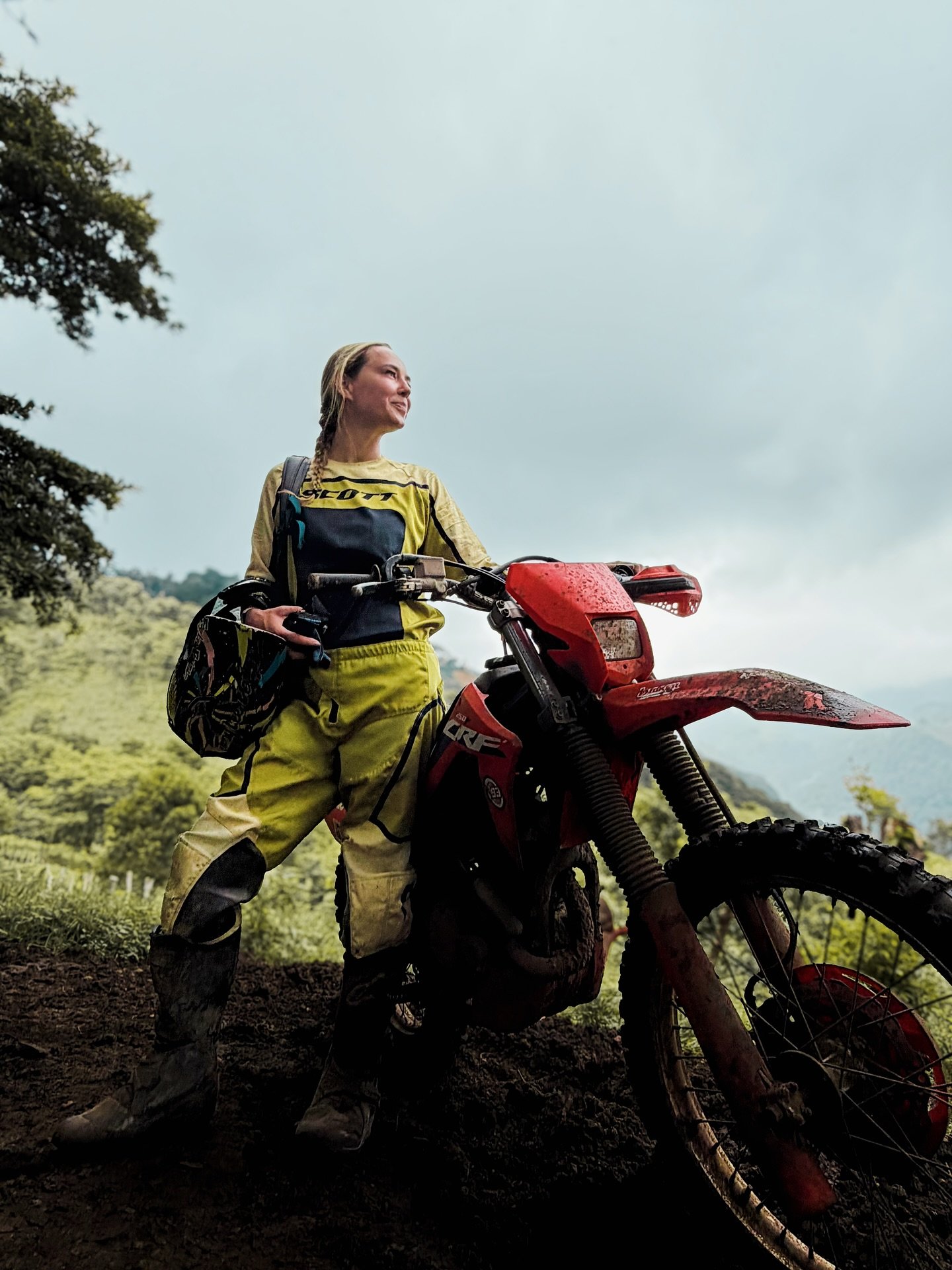 Lindsey standing with her helmet next to a red Honda dirt bike in the mountains of El Salvador