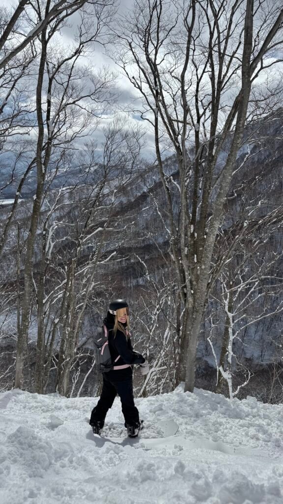 Snowboarder walking through snowy trees in Hakuba