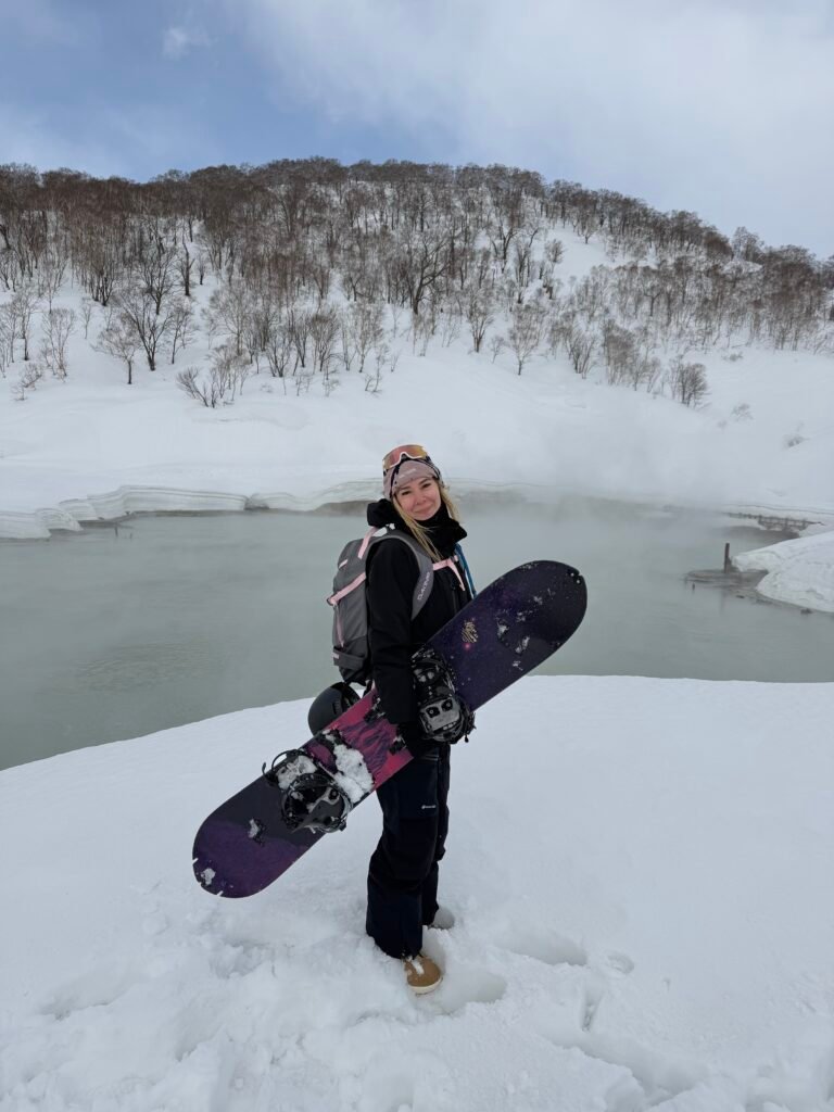 Snowboarder next to a steaming hot spring pond surrounded by snow