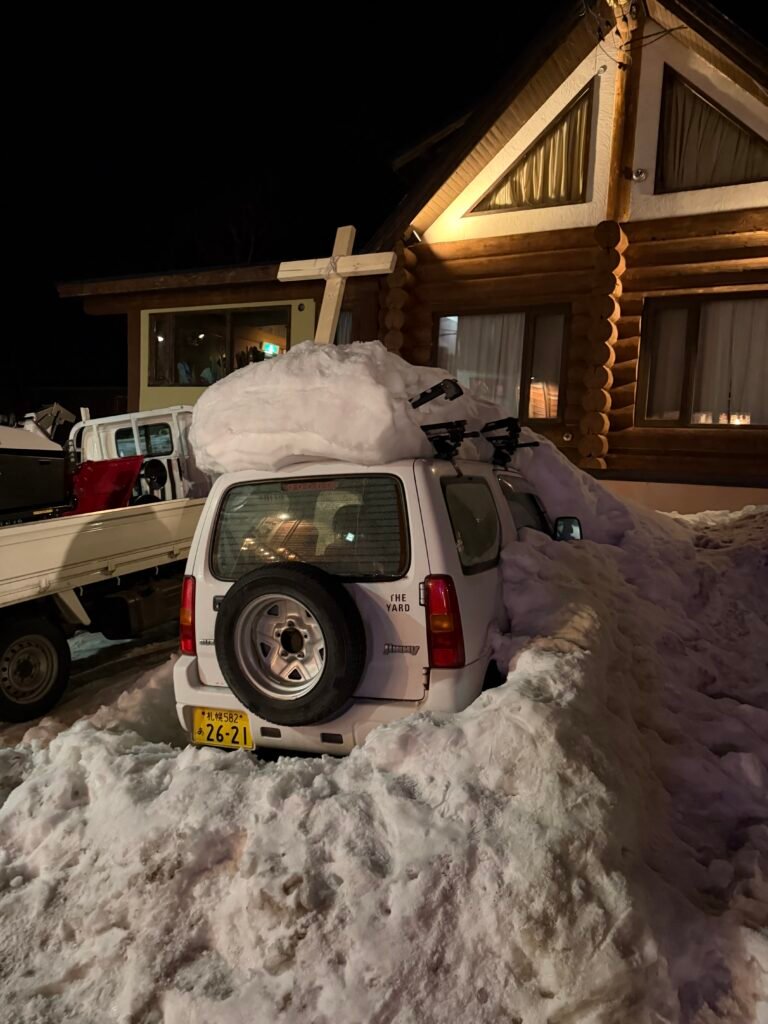 Car buried in a snowbank outside a log house at night