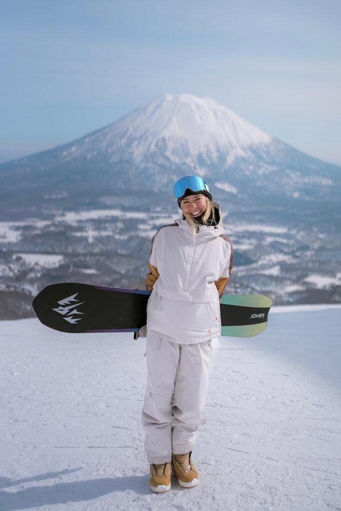 Snowboarder holding her board with Mt. Yotei in the background