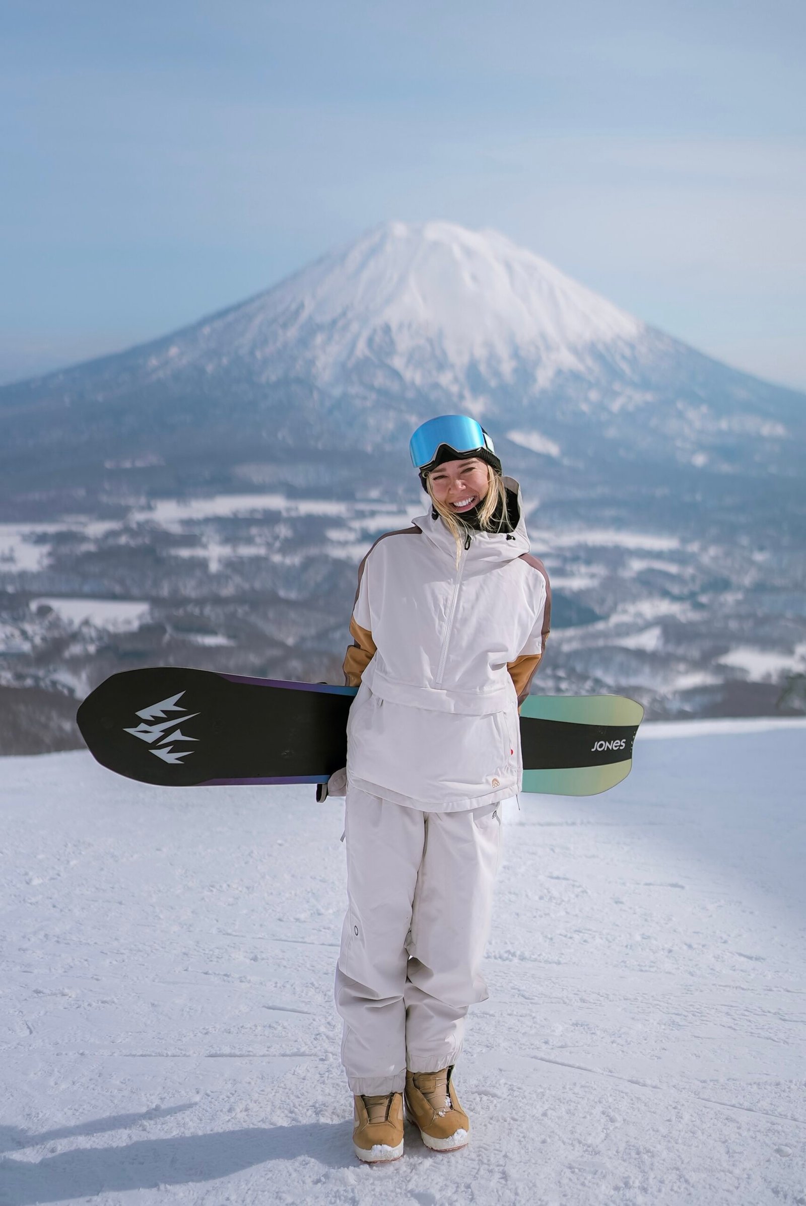 Snowboarder holding her board with Mt. Yotei in the background
