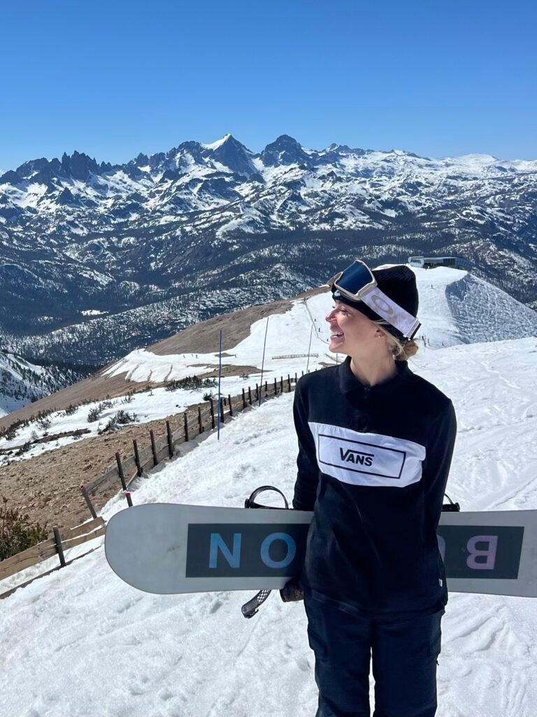 Holding my snowboard on a ridge at Mammoth with snowy peaks behind