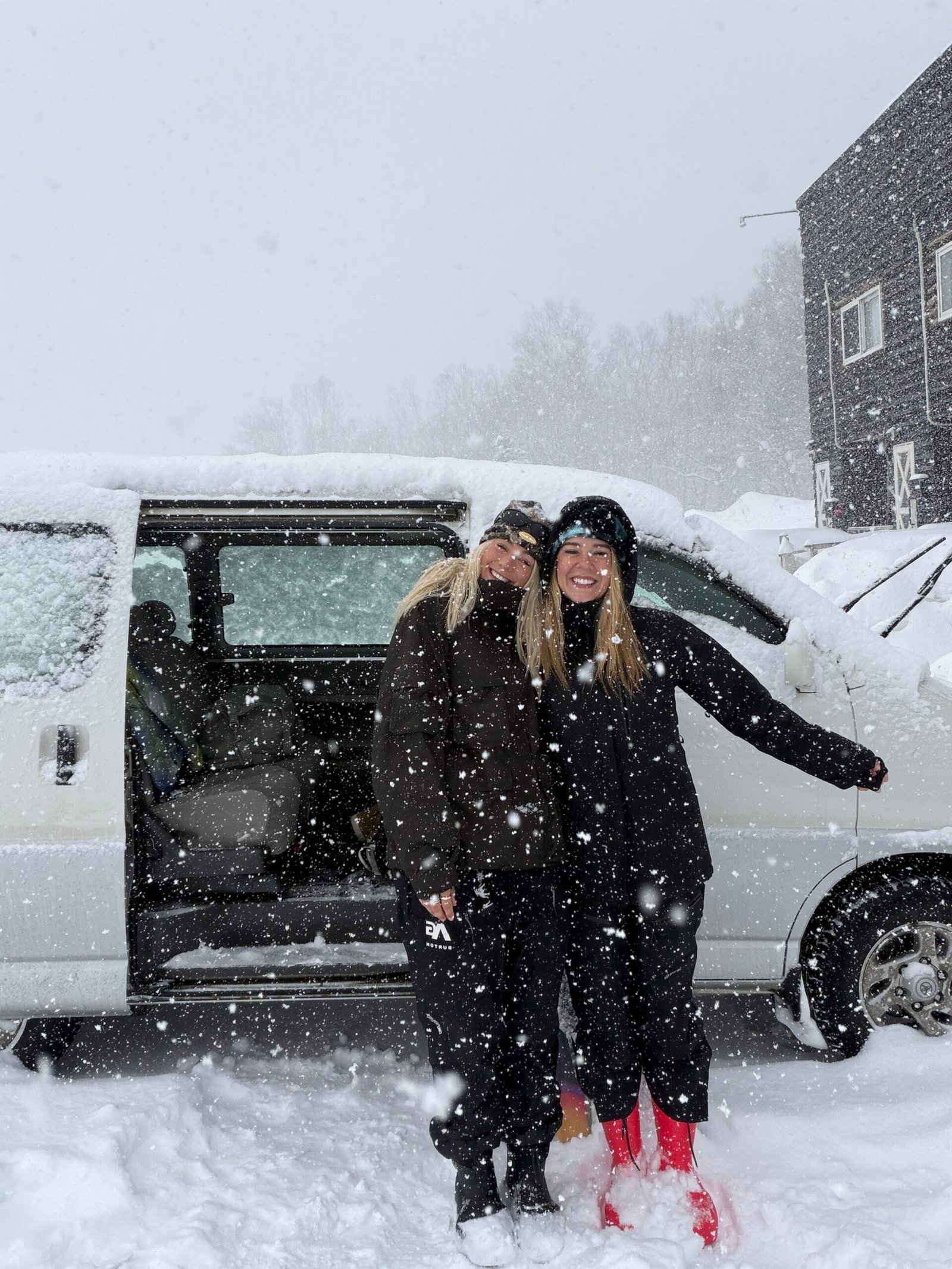 Two friends in snow gear next to a white van in a snowstorm