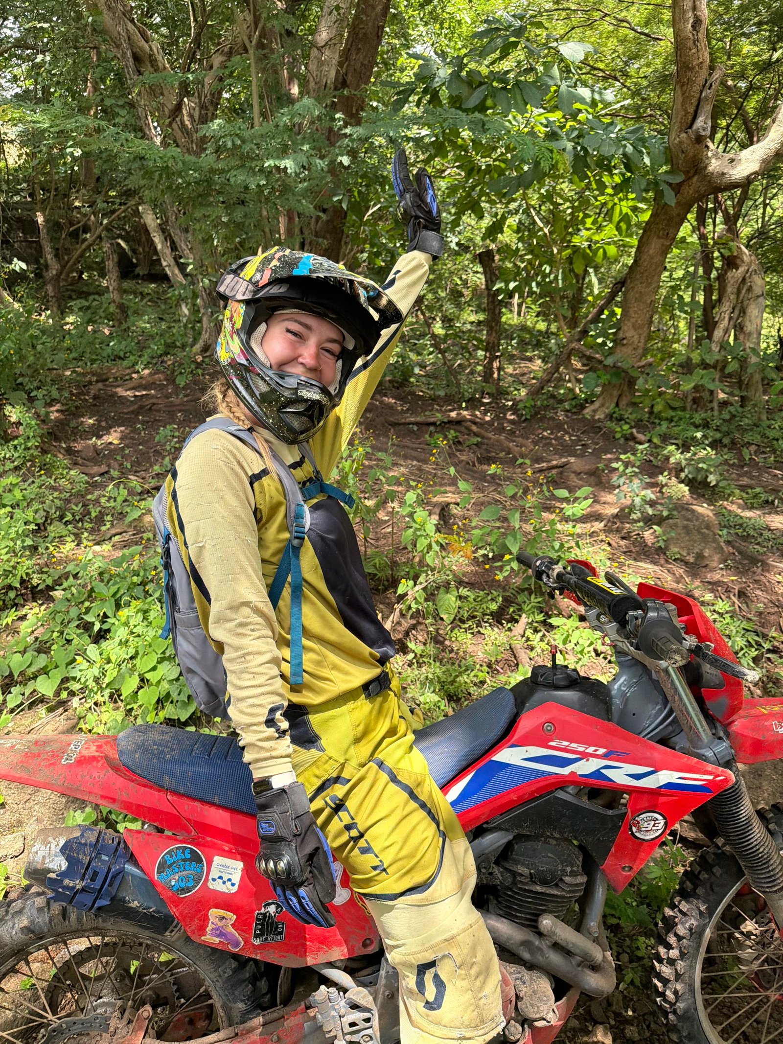Lindsey on a red Honda dirt bike waving in the jungle in El Salvador
