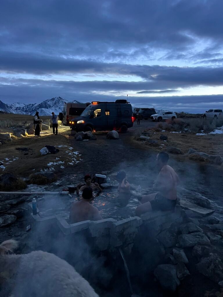 Friends soaking in the small concrete tub at Shepherd Hot Spring at dusk, with the Sierra behind