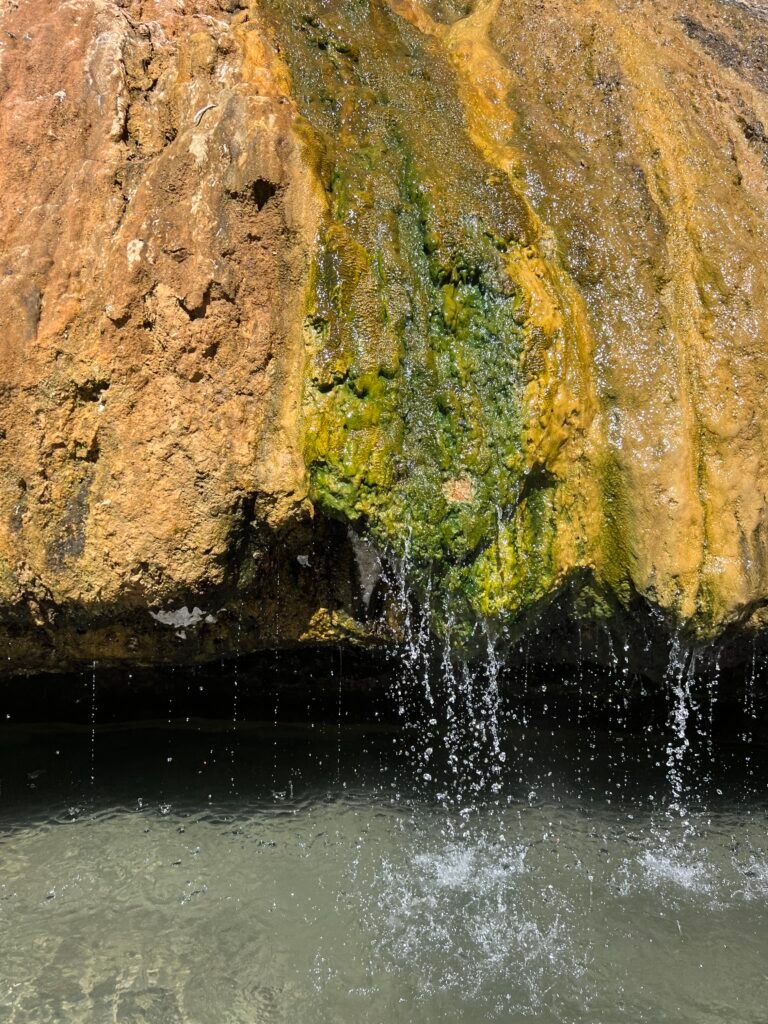 Hot water dripping off the mossy orange rock into the pool at Buckeye Hot Springs
