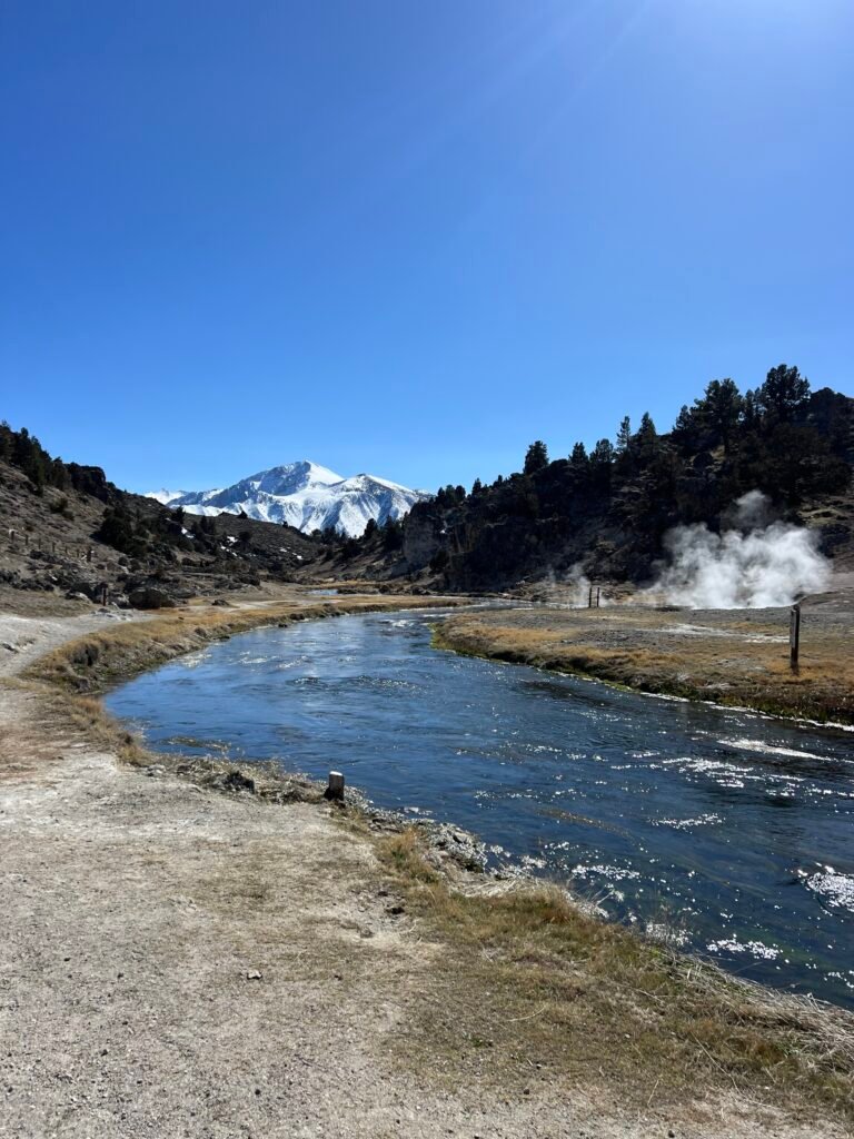Steam rising along a blue creek near Mammoth with snowy peaks behind