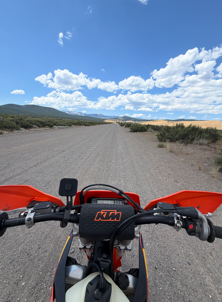 Handlebar view of the KTM on a wide dirt road under a blue sky